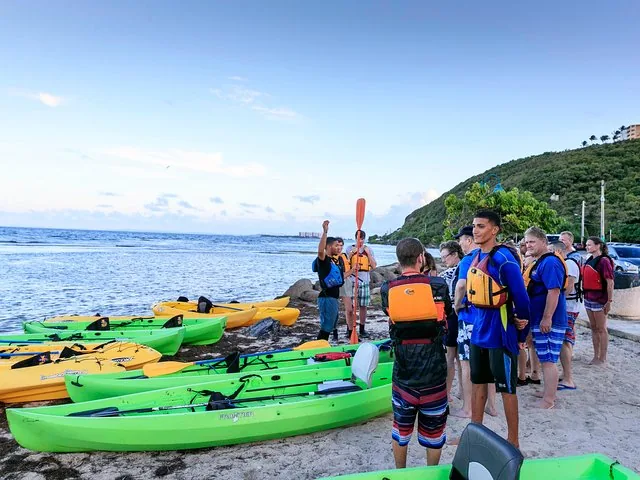Tour guide talking to a group of people on a beach with kayaks.