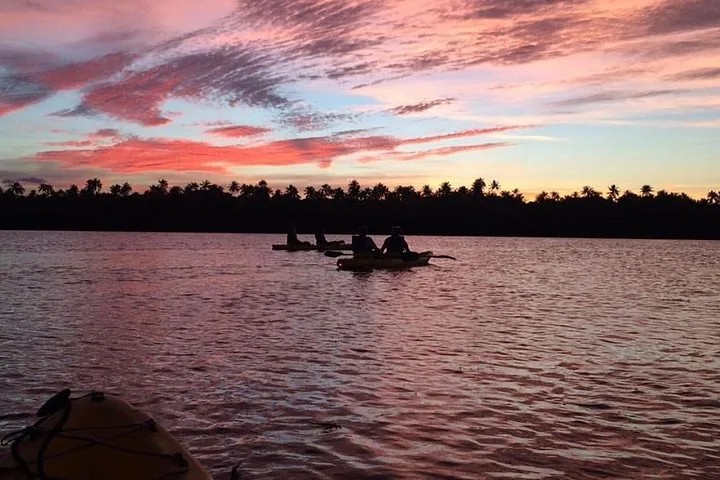 Silhouetten von Menschen beim Kajakfahren auf einem See bei Sonnenuntergang.