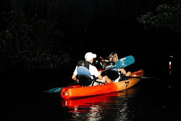 Dos personas remando en kayak de noche con una luz roja que ilumina el agua.